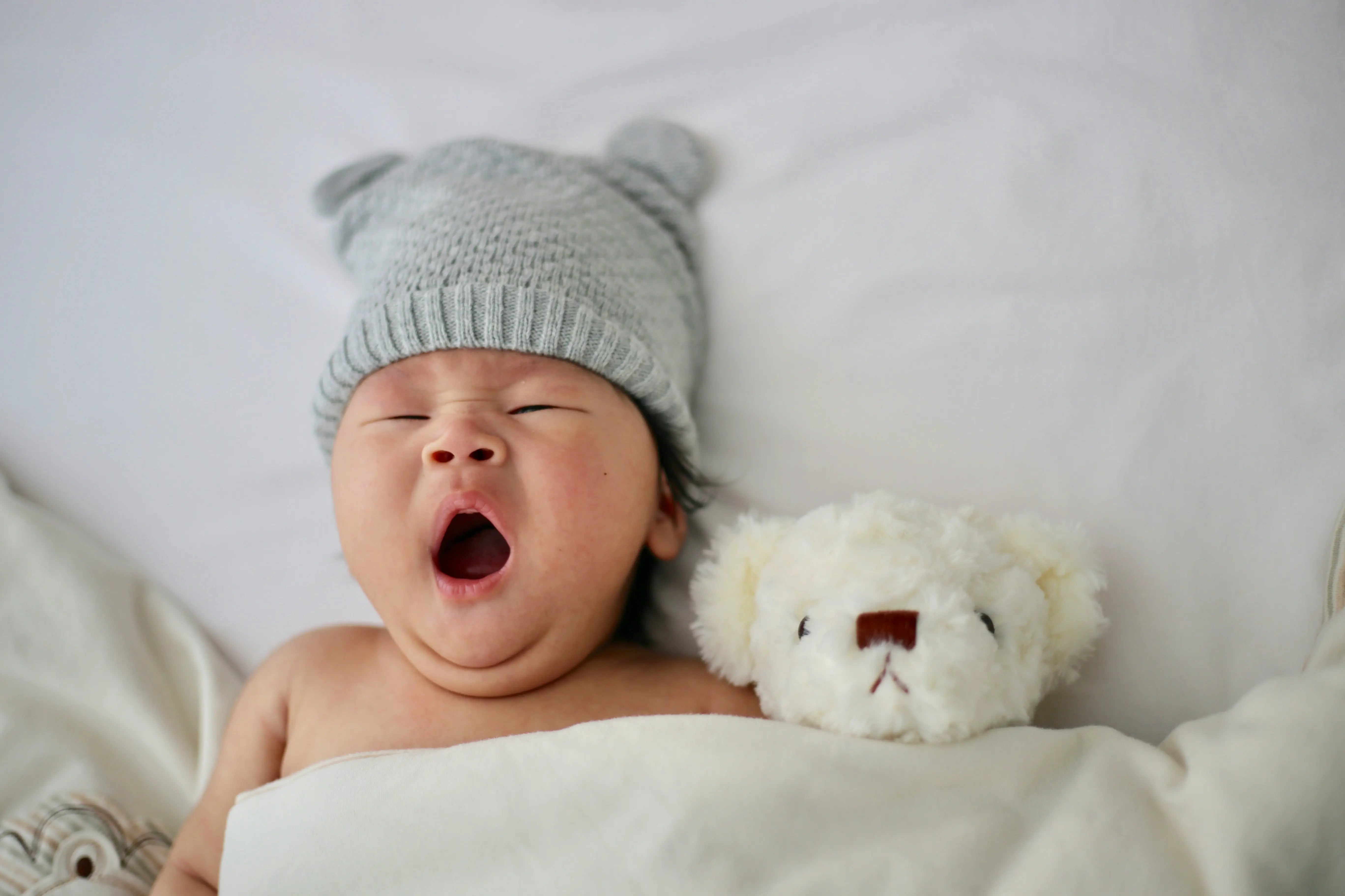 Müdes süßes Baby mit Kuscheltier in einem Bett mit weichen Kopfkissen und Decke.
