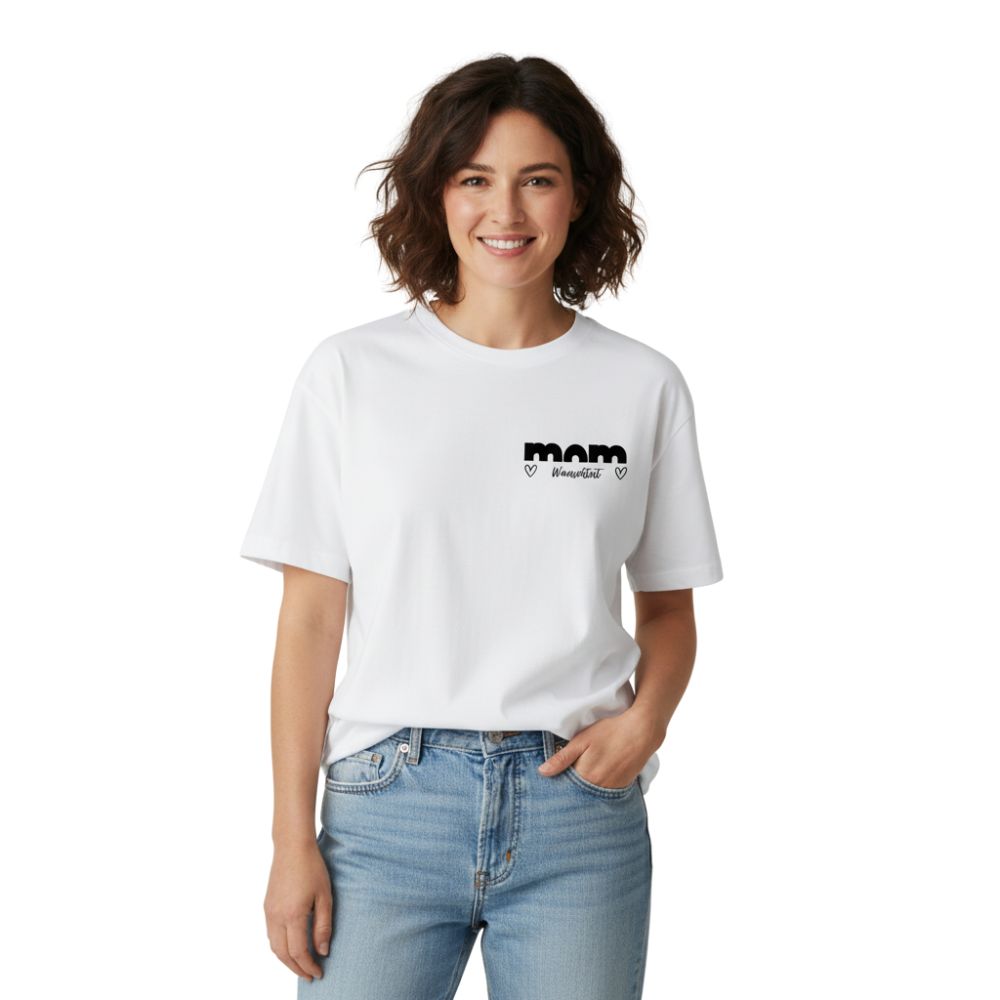 Moderne Mama (32 J.) im weißen Oversize Shirt "MOM TRUE", personalisiert, mit lockerer Jeans vor weißem Hintergrund.
