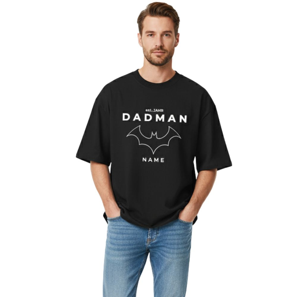 PREMIUM Oversize T-Shirt "DADMAN" (200 g/m² Bio-Baumwolle) in Schwarz. Männliches Model im lässigen Full-Shot, T-Shirt personalisiert. Der Relaxed Fit und die lockere Passform sind gut sichtbar. Hochwertiges Geschenk für Papa.